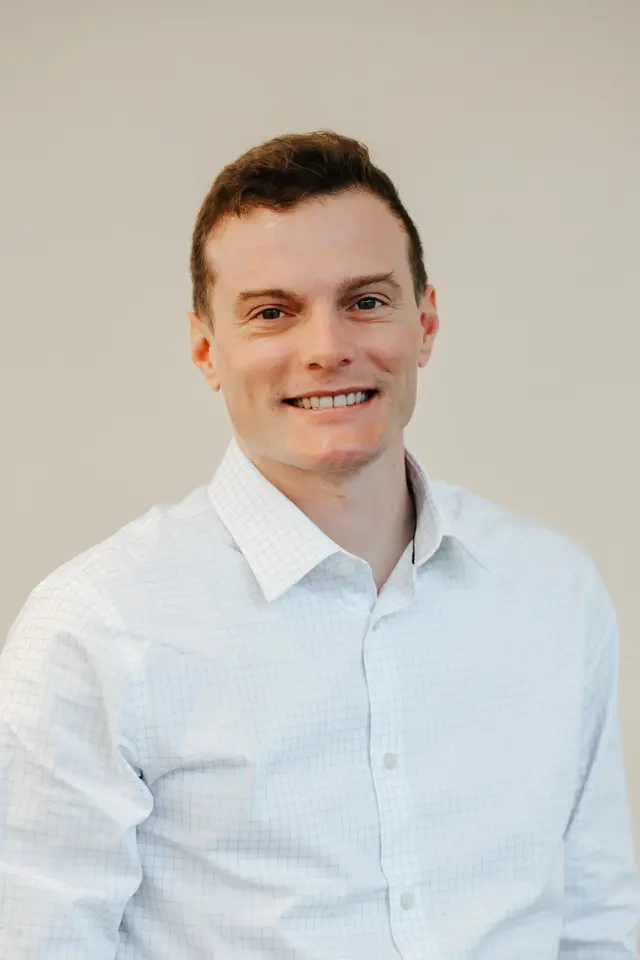 Bryan Basham, smiling, wearing a light checked dress shirt against a neutral background