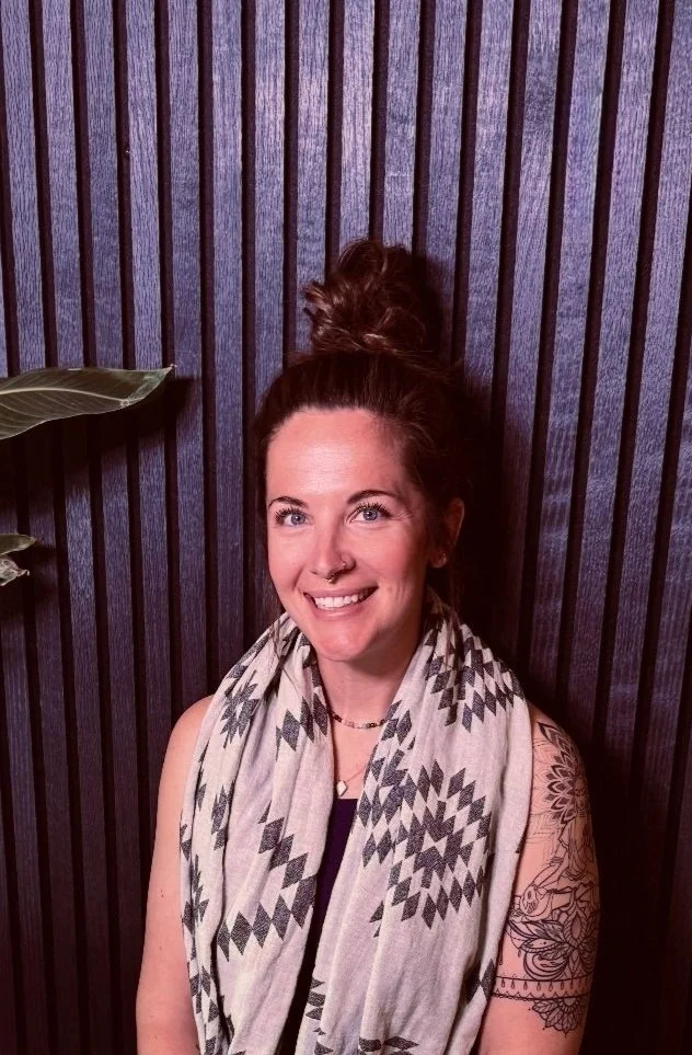 Hayley Bowen, smiling, wearing a patterned scarf in front of a wood slat wall
